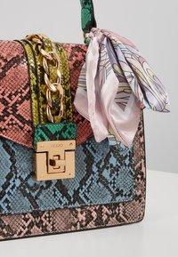 Sac à main coloré à motif peau de serpent, détail chaîne dorée, fermoir doré marqué ALDO, et foulard noué aux motifs pastel rose et violet.