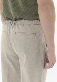 Pantaloni in lino beige chiaro con vita elastica, dotati di due tasche posteriori e una maglia verde testurizzata in vestibilità rilassata.