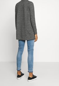Suéter largo de punto gris con un dobladillo asimétrico, combinado con jeans skinny de color azul claro y zapatillas de lona negras. Textura suave, diseño minimalista.