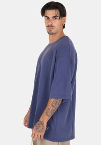 T-shirt oversize a maniche corte di colore blu profondo, realizzato in tessuto morbido. Presenta un collo rotondo e dettagli di cucitura sottili.