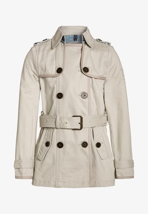 Béžový trenčkot s dvojitými knoflíky, páskem v oblasti pasu, na ramenech a texturovanou tkaninou. Viditeľná modrá podšívka s vzorem.