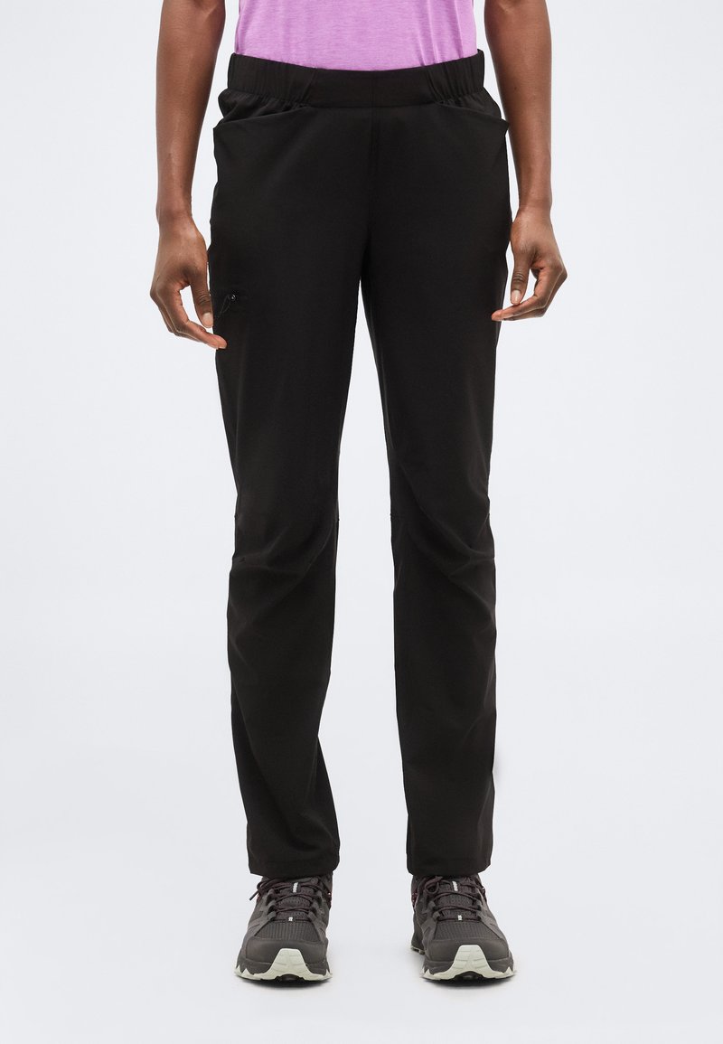 Eespoolt vaadatuna inimene, kes kannab musta elastse vöökohaga pükse küljetaskutega ja halli matkajalatsit, taustal hele ühtlane foon.