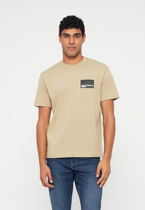 Beige cotton t-shirt with a crew neck and short sleeves. Features a black rectangular patch with white text on the left chest.