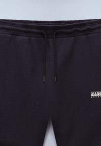 Black sweatpants with an elastic waistband, black drawstrings, and a small white logo patch on the front. Soft cotton blend fabric.