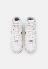 White high-top sneakers with leather and suede materials, perforated toe box, light pink accents, and grey padded collar. Prominent lacing system.