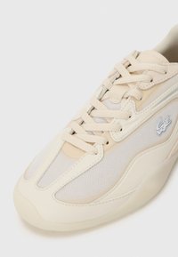 Beige Sneaker mit einer Mischung aus glatten und Mesh-Materialien, runder Zehenpartie, Schnürdesign und einem dezenten Logodetail an der Seite.