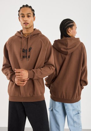 Felpa oversize marrone realizzata in morbido tessuto, con grafica frontale di una farfalla e testo. Maniche lunghe e tasca a marsupio.