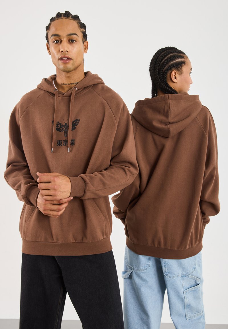 Hnědá oversized mikina vyrobená z měkké látky, s předním potiskem motýla a textem. Dlouhé rukávy a klokanková kapsa.