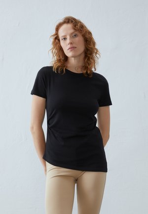 Sort kortærmet t-shirt lavet af blød bomuld, med et klassisk crew neck design. Sammen med lyse beige leggings.