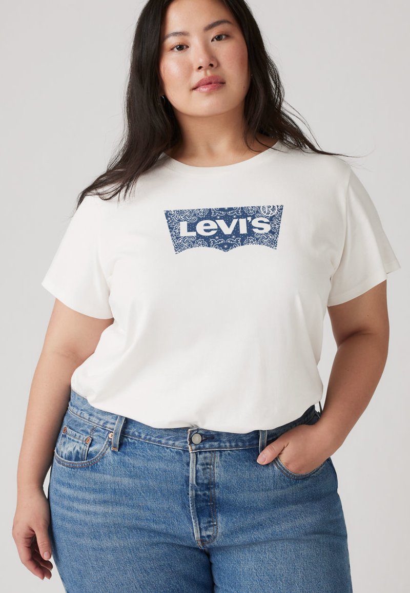 Λευκό βαμβακερό T-shirt με μπλε λογότυπο Levi's με λουλουδάτο μοτίβο· φορεμένο με μπλε ψηλόμεσα τζιν παντελόνια με κλασική εφαρμογή και ανοιχτό πλύσιμο.