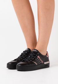 Schwarze Ledersneaker mit Plateausohle, runder Spitze, schwarzen Schnürsenkeln und pinken Leopardenmusterakzenten mit Nieten an den Seiten.