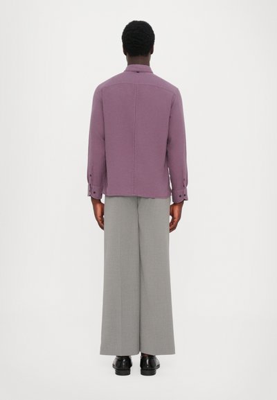 Lilla skjorte med lange ærmer, kombinert med lysegrå vide bukser. Outfitet har et minimalistisk design og en glatt tekstur.