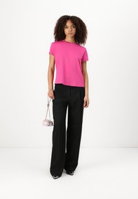 T-shirt fucsia a maniche corte con una vestibilità rilassata, abbinata a pantaloni neri a righe sottili. Il modello tiene in mano una piccola borsa rosa chiaro.
