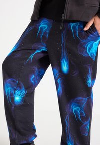 Sorte sweatpants med en livlig blå vandmandemønster, med en glat tekstur og en kontrasterende kosmisk stjernebagtgrund. Inklusive elastisk taljebånd.