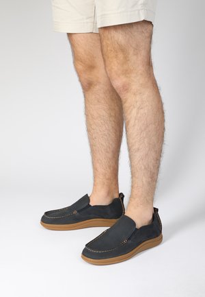 Marine slip-on sko med overdel i ruskind, kontrasterende syninger og en tan gummisål. Med en lavprofil design og minimalistiske detaljer.