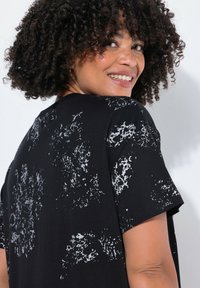 T-shirt noir à manches courtes présentant un motif abstrait gris texturé, fabriqué en tissu doux, avec un col rond et une coupe décontractée.