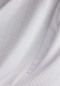 Hvit stoff med en glatt tekstur, med et subtilt geometrisk mønster og variert glans. Inkluderer lagdelte seksjoner og myke draperinger.
