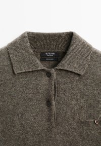 Kasjmier poloshirt in een gedempte bruine kleur. Voorzien van een kraag, een knoopsluiting met drie knopen en één zak. Zachte, getextureerde brei.