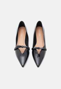 Μαύρα γυναικεία παπούτσια μυτερά από συνθετικό δέρμα με σχέδιο κοψίματος και λεπτό διακοσμητικό λουράκι πάνω από το κουντεπιέ. Ομαλή υφή με ελάχιστα μεταλλικά στοιχεία.