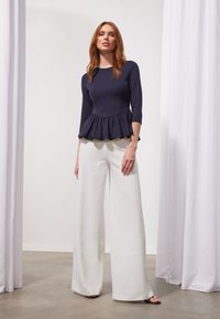Tumes peplum tops, mille ümar kaelus ja kolmeveerandi varrukatega, on kombineeritud laia jalgadega valgete pükstega ja mustade libisemisjalatsitega. Siledad tekstuurid.