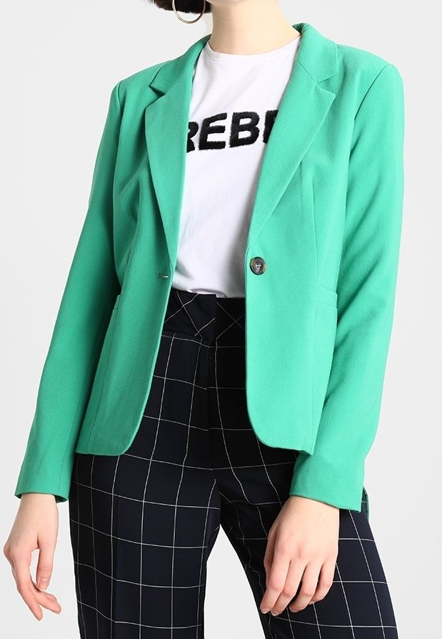 Blazer vert menthe avec une coupe ajustée et un col à revers. Présente un bouton unique et est porté par-dessus un t-shirt blanc et un pantalon à carreaux.