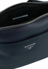 Navy blauer synthetischer Clutch mit Reißverschluss, ausgestattet mit einer strukturierten Oberfläche und silbernen Beschlägen. Das Innere enthält ein Logotag und eine Stoffauskleidung.