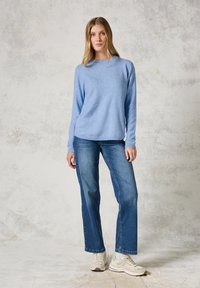 Helles blaues Langarmpullover mit Rundhalsausschnitt, kombiniert mit blauen Jeans im geraden Schnitt und beigen Sneakers. Weiche Textur, lässiges Design.