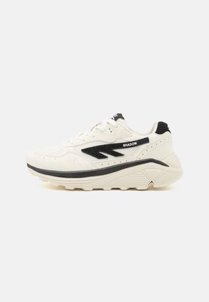 Sneaker di colore crema chiaro con dettagli neri, tessuto testurizzato e suola spessa. Presenta perforazioni, un logo e un design con lacci.