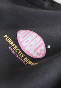 Black fabric garment featuring a graphic design with a pink oval "Bubbles" logo, white lettering, and yellow text below.