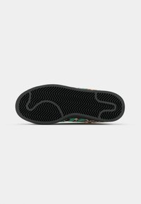 Sneaker con suola in gomma nera testurizzata con motivo a spina di pesce, dettagli verdi e tomaia con stampa leopardata.