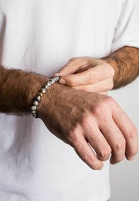 Krelles rotas, kas veidotas no melnā un baltā plankumainā akmens maisījuma, ar vienu zeltainu akcenta krelli, uz rokas, kurai redzami mati.
