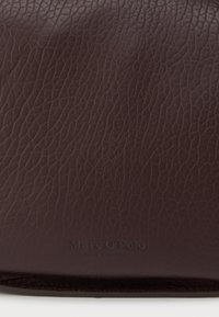 Temno rjav teksturiran usnjen površinski sloj z nežno vtisnjeno blagovno znamko Marc O'Polo blizu spodnje robove.