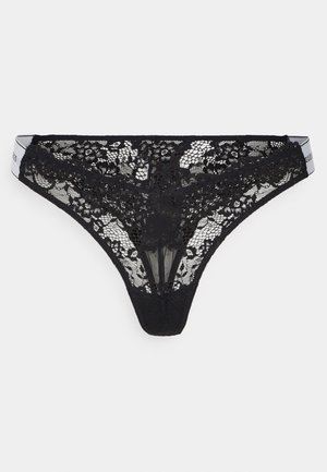 Black lace thong featuring floral patterns, sheer texture, and a contrasting waistband with logo detail. Cut low for minimal coverage.