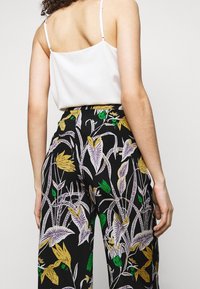 Blommönstrade byxor i svart med gula, lila och gröna accenter; kombinerat med en vit satin-camisole med tunna band.