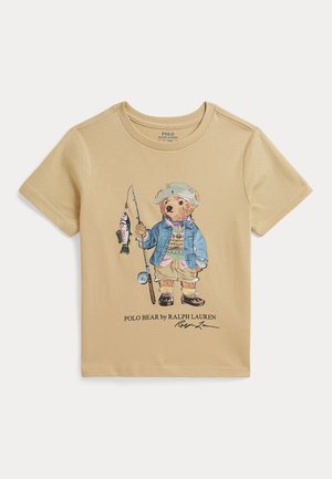 Beżowy t-shirt z niedźwiedziem ubranym w sprzęt wędkarski, trzymającym wędkę z złowioną rybą, z napisem „Polo Bear by Ralph Lauren”.