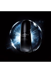 Svart flaske med Shiseido Men Ultimune Power Infusing Serum, sylinderformet med glatt finish og hvit tekst, omkranset av en strålende blå aura.