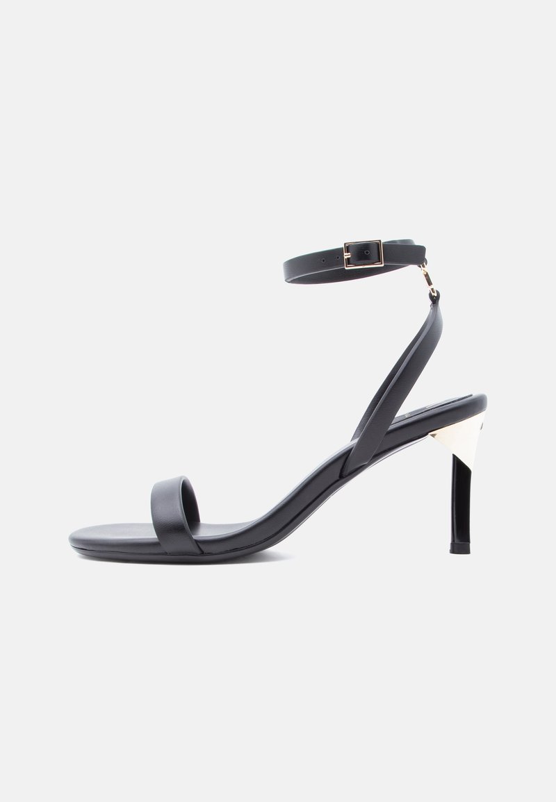 Μαύρο σανδάλι με λουράκια, ψηλό τακούνι, αγκράφα στον αστράγαλο, λεπτό τακούνι και ανοιχτή μύτη σε λευκό φόντο.