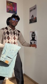 Šviesiai mėlynas džinsinis švarkas, derinamas su smėlio spalvos ir rudos argyle rašto megztiniu. Taip pat dėvimi juodi džinsai, akiniai ir kepurė.