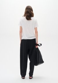 Tricou alb cu mânecă scurtă, pantaloni negri largi, geantă din piele neagră netedă. Persoana stă cu spatele la cameră pe un fundal simplu.