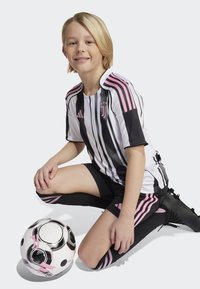 Maillot de football des jeunes de la Juventus avec un maillot rayé noir et blanc avec des accents roses, un short noir et un ballon de football noir avec des détails roses.