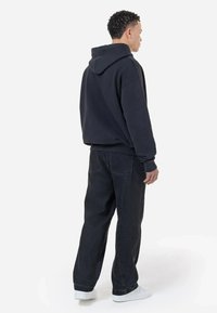 Sudadera negra con bolsillo canguro, tela texturizada, corte holgado, combinada con pantalones de mezclilla oscuros, con un corte relajado y bolsillos traseros.