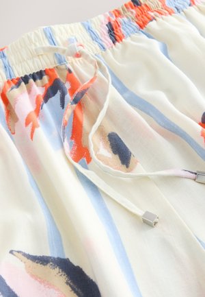 Gros plan d’un tissu avec taille élastique et cordon, présentant des motifs floraux abstraits et des rayures en crème, bleu, orange et bleu marine.