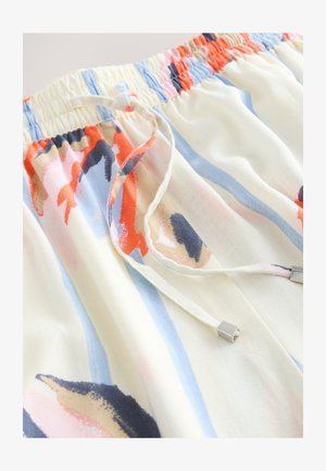 Gros plan d’un tissu avec taille élastique et cordon, présentant des motifs floraux abstraits et des rayures en crème, bleu, orange et bleu marine.