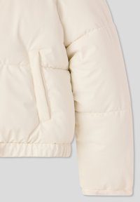 Puszysty kremowy rękaw kurtki o fakturowanym wykończeniu, z boczną kieszenią i elastycznym mankietem u dołu dla wygodnego dopasowania.