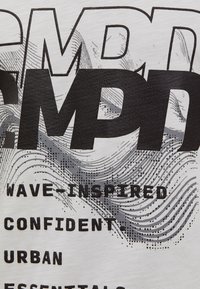 White short-sleeve shirt featuring bold black text with wave-like gray graphics, highlighting the words "WAVE INSPIRED," "CONFIDENT," and "ESSENTIALS."