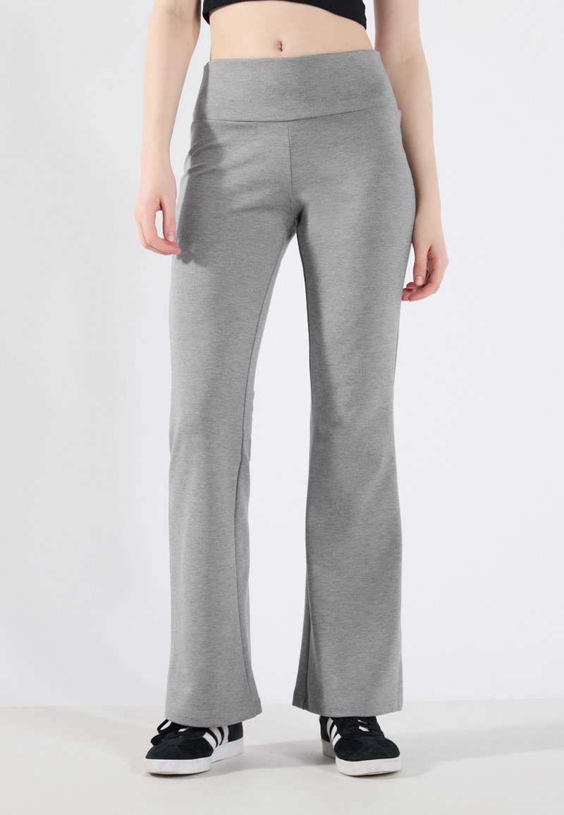 Grå flared bukser laget av elastisk stoff, med bred midjebånd og glatt tekstur, kombinert med svarte joggesko.