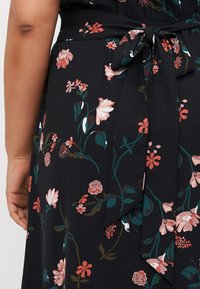 Black fabric dress with a floral pattern in pink and green. Features a tied waist belt and short sleeves with a relaxed fit.