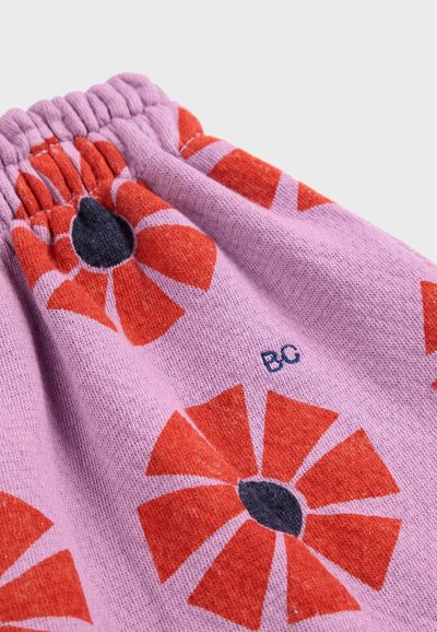Erschwinglicher lila Stoff mit rotem Blumenmuster, das schwarze Mittelpunkte aufweist. Elastischer Bund, weiche Textur und sichtbare Markeninitialen.