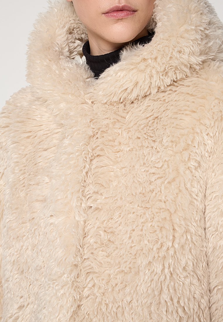 Beige Kapuzenmantel aus Kunstfell mit einer weichen, strukturierten Oberfläche und großer Kapuze. Verfügt über einen Frontverschluss und eine lockere Passform.