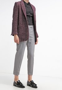 Blazer texturizado de color rosa oscuro, camisa negra, pantalones a medida gris claro y mocasines negros brillantes con borlas. Nota: bolsillos delanteros dobles en el blazer.